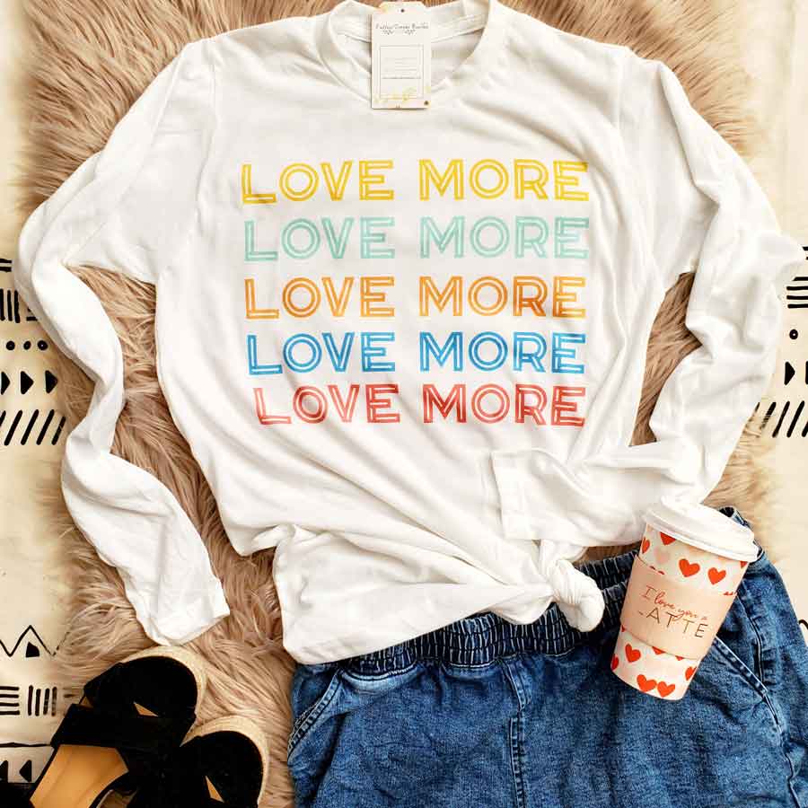 White color long sleeve graphic tee with multi-color quote "Love More".